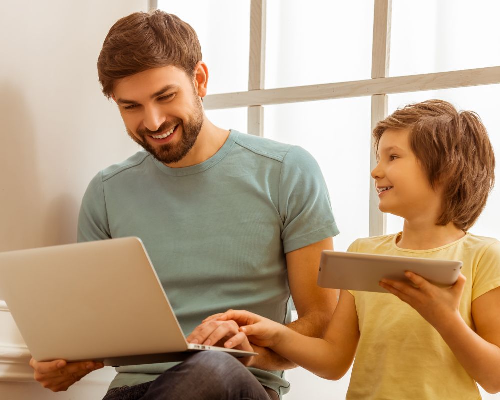 Padre e hijo con un portátil y tablet mirando contenidos digitales.